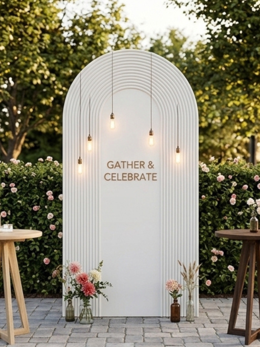 Modern wedding arch backdrop idea featuring a white textured arch, vintage string lights, and lush floral arrangements for outdoor reception photo booths.